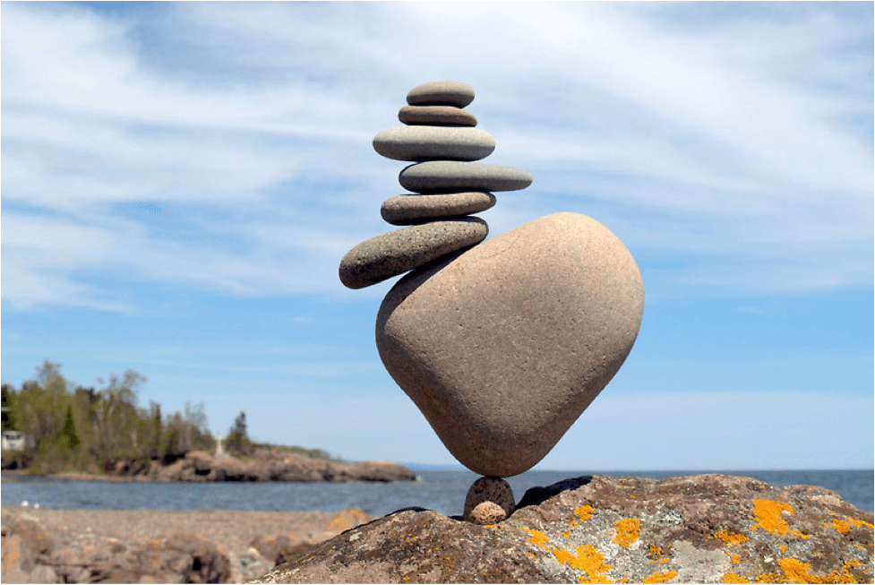 Image of 8 rocks of varying sizes stacked on top of eachother precariously on a beach